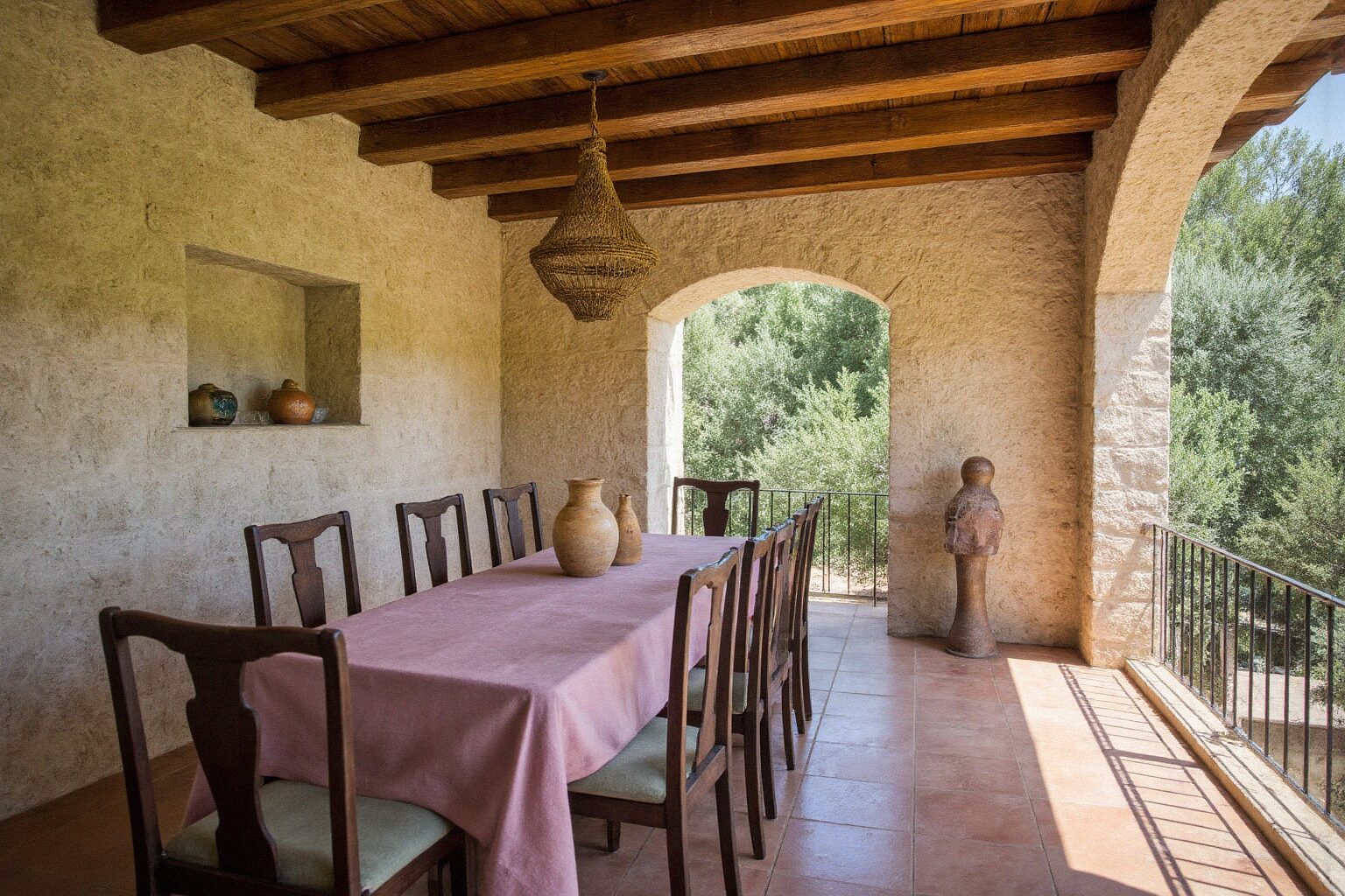 Covered Mediterranean terrace at golden hour with terracotta floor, sheer white curtains and a set dining table